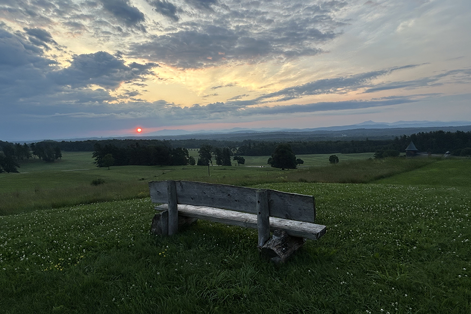 sunrise over green mountains; bench in foreground