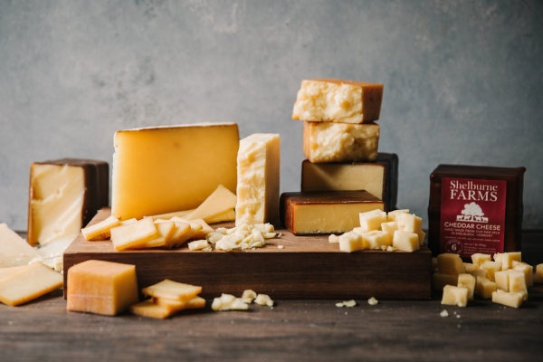 Various types of Shelburne Farms cheddar are arranged on a wooden cheese board.